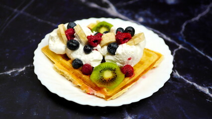 Waffles with whipped cream, blueberries, bananas, raspberries, and kiwi