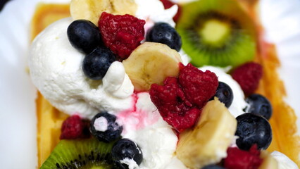 Waffles with whipped cream, blueberries, bananas, raspberries, and kiwi
