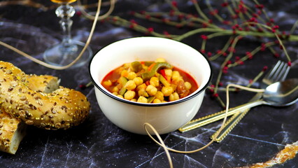 Dish with chickpeas, peppers, carrots and other vegetables with a whole grain roll and a glass of wine
