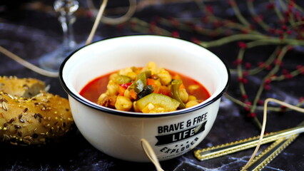 Dish with chickpeas, peppers, carrots and other vegetables with a whole grain roll and a glass of wine
