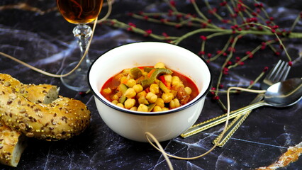 Dish with chickpeas, peppers, carrots and other vegetables with a whole grain roll and a glass of wine
