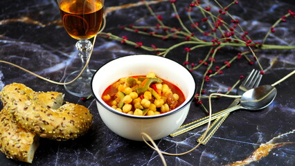 Dish with chickpeas, peppers, carrots and other vegetables with a whole grain roll and a glass of wine
