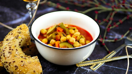 Dish with chickpeas, peppers, carrots and other vegetables with a whole grain roll and a glass of wine
