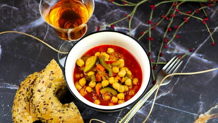 Dish with chickpeas, peppers, carrots and other vegetables with a whole grain roll and a glass of wine
