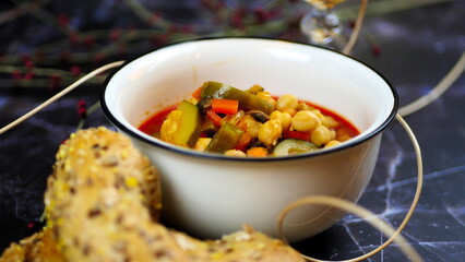 Dish with chickpeas, peppers, carrots and other vegetables with a whole grain roll and a glass of wine
