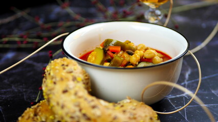 Dish with chickpeas, peppers, carrots and other vegetables with a whole grain roll and a glass of wine
