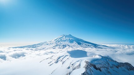 A photo of an isolated snow covered volcano taken from the air, with a clear blue sky and white clouds below it