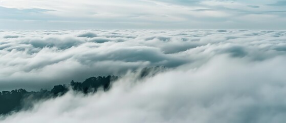 Fototapeta premium An endless sea of clouds blankets the landscape, with mist-shrouded peaks peeking through, creating a mystical and ethereal atmosphere.