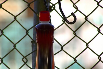 bottle of syrup hanging from a chain link fence