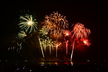 Colorful fireworks celebration with people and the city night light background at the seaside. International firework festival at Pattaya, Thailand.