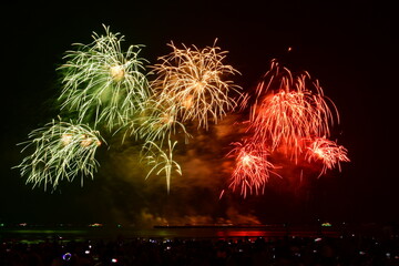 Colorful fireworks celebration with people and the city night light background at the seaside. International firework festival at Pattaya, Thailand.