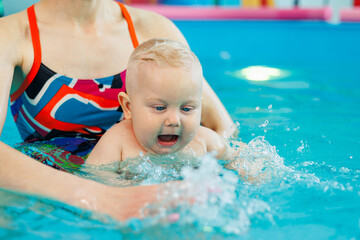 A baby learns to swim in a pool with a trainer. Children's pool. Swimming courses for children.