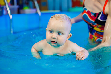 A baby learns to swim in a pool with a trainer. Children's pool. Swimming courses for children.