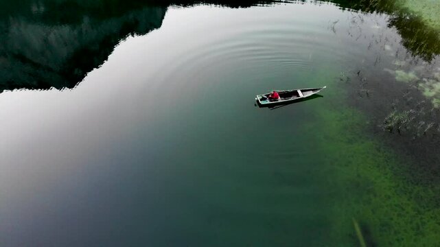 The fisherman in the boat on the green lake