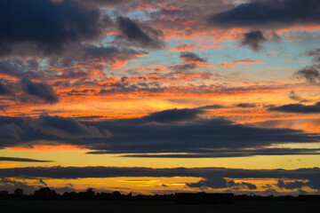 Fototapeta premium Vibrant Sunset Sky with Yellow and Blue Clouds Over a Tranquil Field