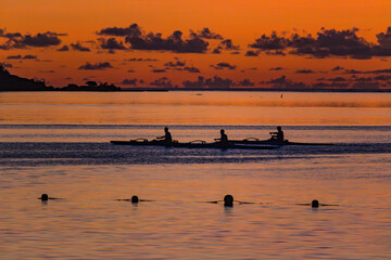 The image captures a serene sunset scene in Morea, near Tahiti, the sky is painted in vibrant shades of orange, with scattered clouds adding texture to the horizon.