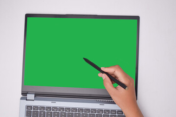 Close-up of a hand holding a stylus, pointing at a blank green screen on a laptop. set up for...