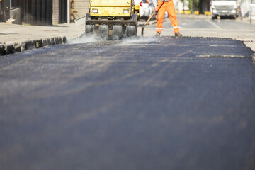Construction workers paving a new asphalt road on a city street during the day with machinery in use
