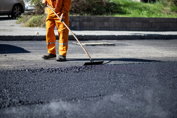 Road worker applying fresh asphalt on a sunny day in a city street, focusing on surface repair and...