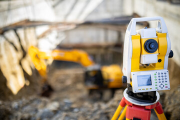 Surveying equipment focused in the foreground with an excavator working in a construction site...