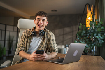 Portrait of man with headphones sit at work desk and use cellphone