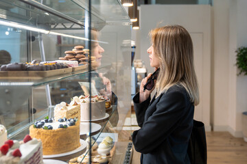 Thoughtful middle aged businesswoman choosing desserts in modern bakery for coffee break near...