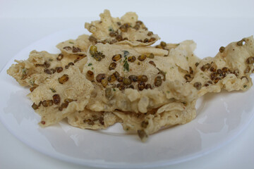 Traditional crackers with mung bean sprinkles from Indonesia, called Rempeyek Kacang Hijau. On white plate, isolated on white background