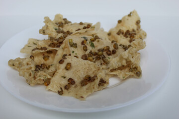 Traditional crackers with mung bean sprinkles from Indonesia, called Rempeyek Kacang Hijau. On white plate, isolated on white background
