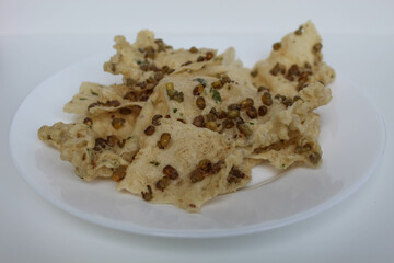 Traditional crackers with mung bean sprinkles from Indonesia, called Rempeyek Kacang Hijau. On white plate, isolated on white background