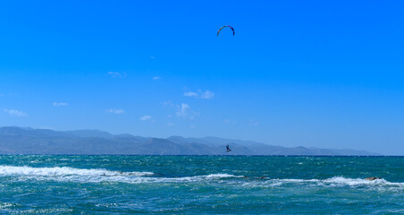 Kite surfer glides through vibrant blue waters under a clear sky at the coast during a sunny afternoon adventure