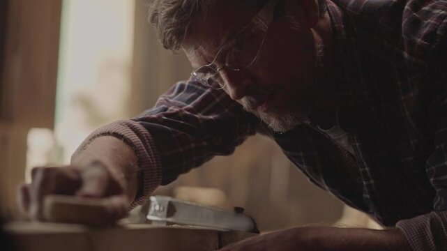Close-up shot of a carpenter or joiner sanding wooden plank with sanding paper in wood workshop. Shot in slow-motion