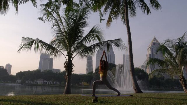 Serene shot of a yoga instructor practicing mindfulness and balance in Thailand's Rama IX Park, Bangkok. Framed by a massive cascading fountain, the instructor performs a graceful yoga pose on lush gr