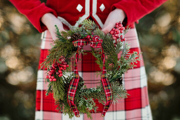 Highland dancer in red and white kilt and red jacket holding a winter wreath.