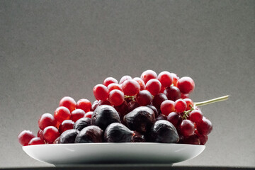 Close-up of plate filled with fresh red grapes and figs against neutral background
