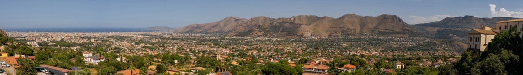 Fototapeta premium Panoramic view of valley dotted with houses, framed by towering mountains and historic buildings perched on hill