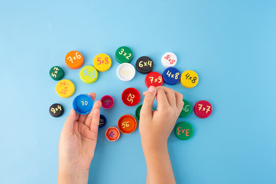 Childrens hands placing colorful caps with multiplication problems on blue background, engaging math game for kids, multiplication table learning tool, math practice concept, educational flat lay,