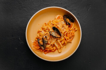 Tagliatelle pasta with mussels and rich tomato sauce in a beige bowl on a dark textured background
