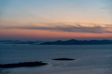 Obraz premium Serene sunset view over tranquil sea and silhouette of islands with vibrant sky colors, showcasing peaceful twilight and natural beauty.