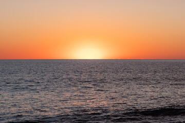 Obraz premium Stunning sunset over the tranquil ocean horizon, casting vibrant orange and yellow hues in the evening sky near the coast