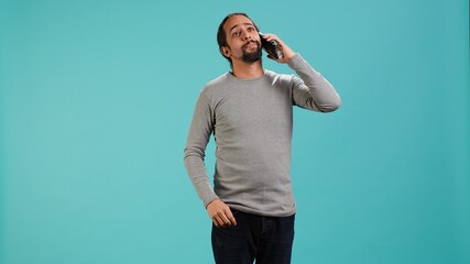 Joyous man catching up with friends in phone call using cellphone, studio background. Portrait of radiant person having conversation with mates during telephone call, camera A