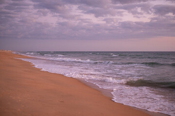 Calm waves lapping at the sandy shore during twilight with a cloudy sky along the coastline