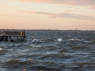 A stunning and beautiful sunset view showcases a lovely pier along with the restless ocean waves crashing