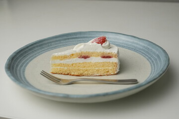 One small Japanese strawberry shortcake and a big fork on a stylish big plate on a white table