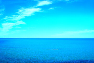Peaceful scenery from Numana Alta with a vision of the vast Adriatic Sea and its slightly rippling waters crossed by a motorboat leaving a foamy white trail on their blue waves and a cyan horizon