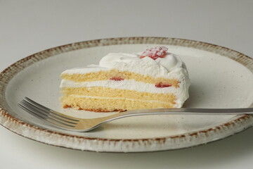 One small Japanese strawberry shortcake and a big fork on a stylish big plate on a white table