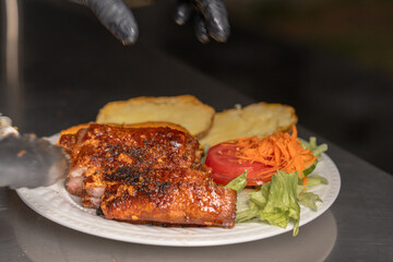 Chef serving grilled meat with potatoes and salad on white plate