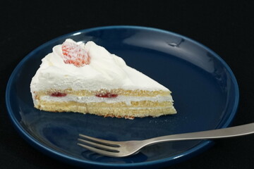 One small Japanese strawberry shortcake on a stylish Japanese plate and fork on a black cloth on a white table
