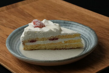 One small Japanese strawberry shortcake on a stylish Japanese plate on a wooden tray on a black cloth on a white table