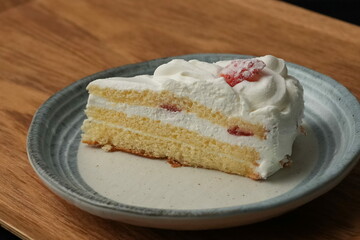 One small Japanese strawberry shortcake on a stylish Japanese plate on a wooden tray on a black cloth on a white table