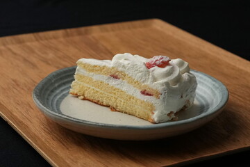 One small Japanese strawberry shortcake on a stylish Japanese plate on a wooden tray on a black cloth on a white table
